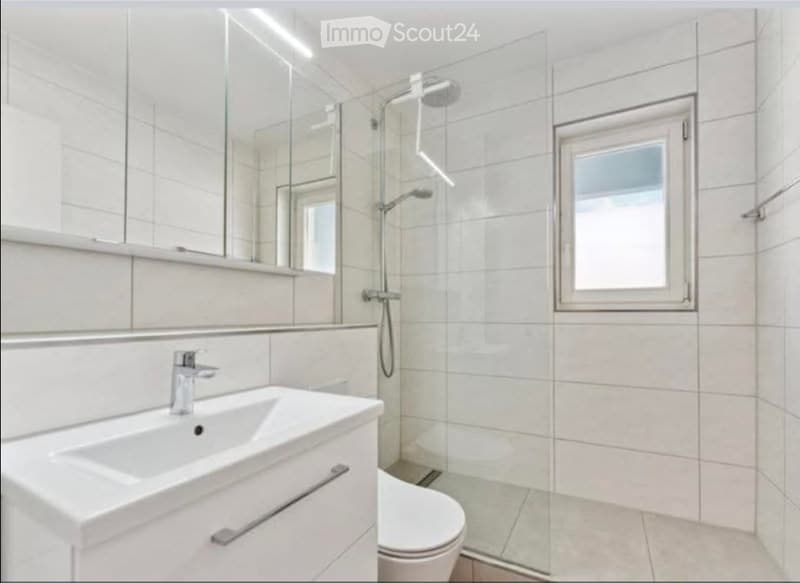 Modern bathroom with white tiles, a large mirror, a glass-enclosed shower, a sink with a modern faucet, and a toilet.