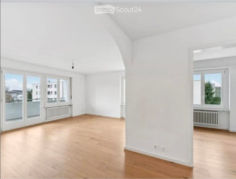 Empty room with light wooden flooring, white walls, large windows, and radiators. No furniture or equipment present.
