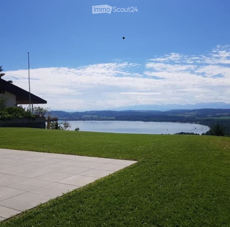 Lush green lawn with a paved patio area, overlooking a scenic lake and distant mountains under a clear blue sky.