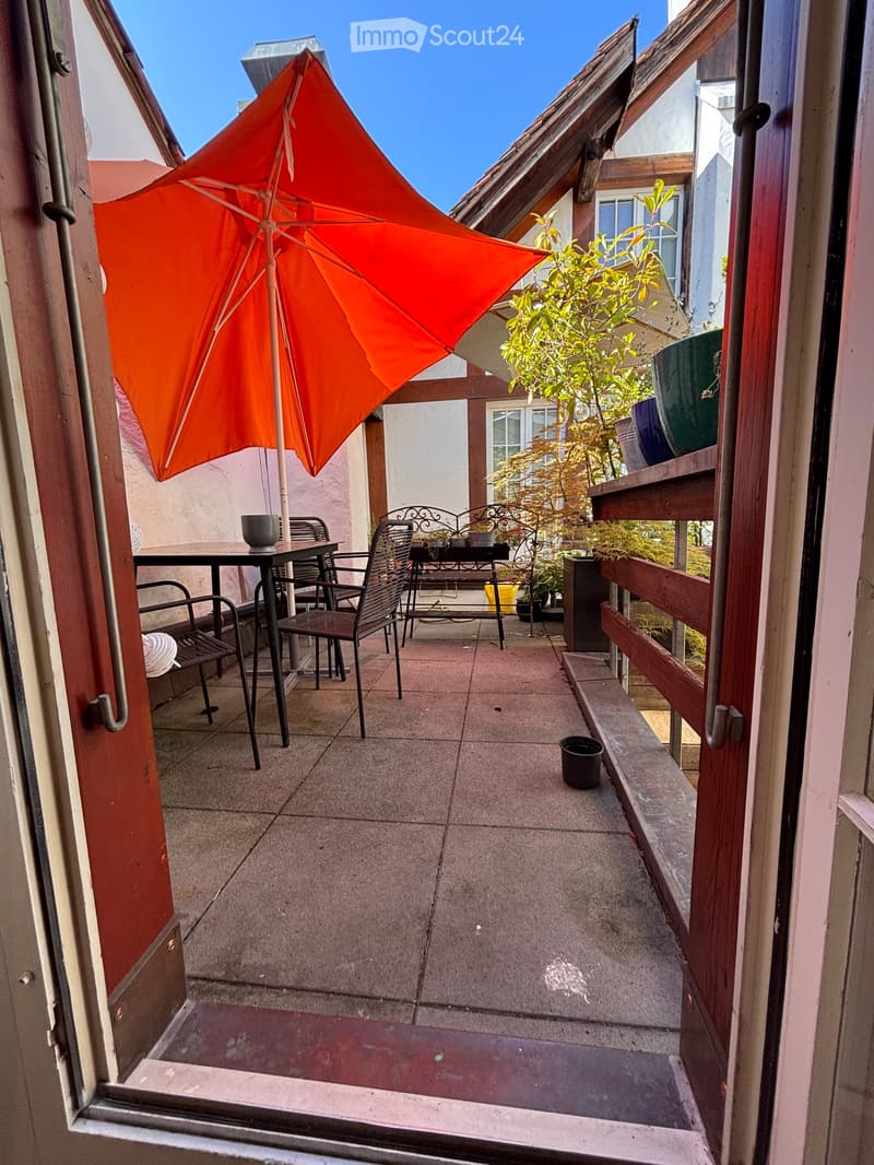Balcony with tiled floor, wooden railing, outdoor table and chairs, and an umbrella.