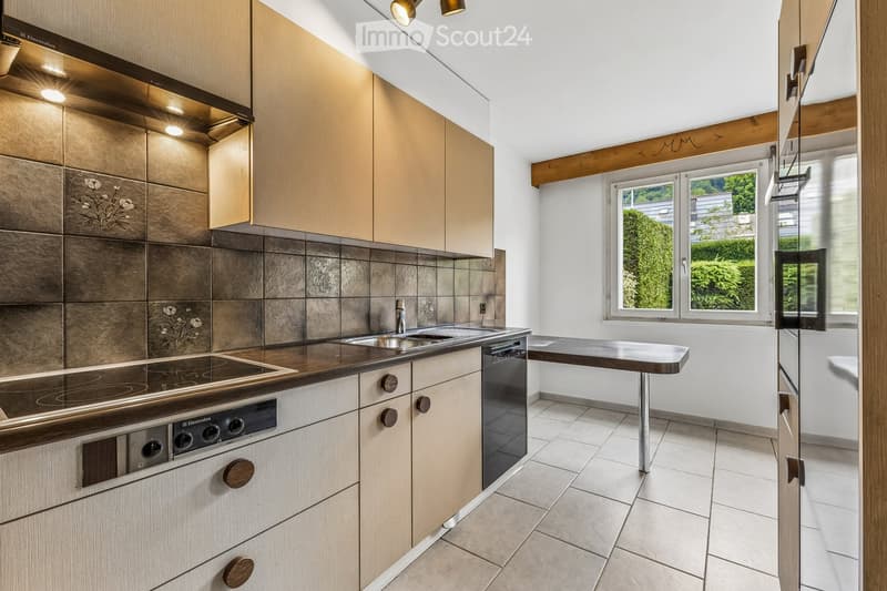 Modern kitchen with light wooden cabinets, stainless steel appliances, and a central island table.