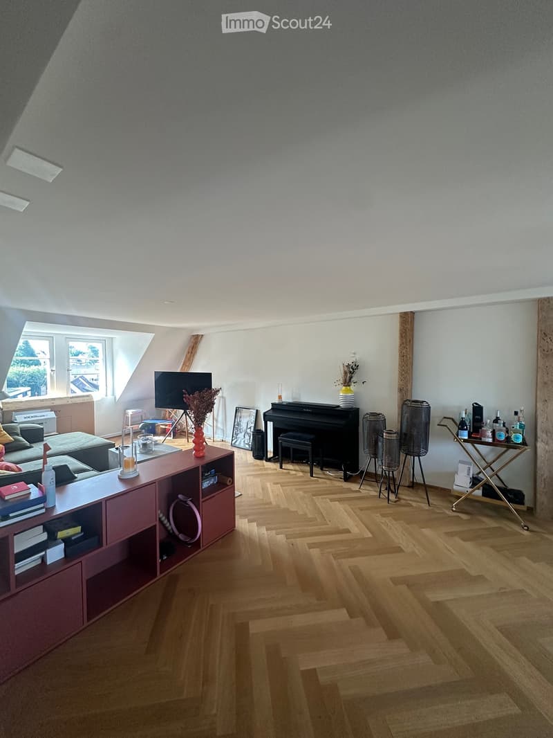 A modern, well-lit living room with wooden flooring, a red cabinet, a sofa, a piano, and decorative items.