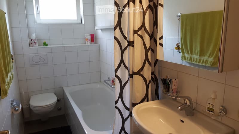 Bathroom with white tiled walls, bathtub, toilet, sink, shower curtain, and various toiletries.