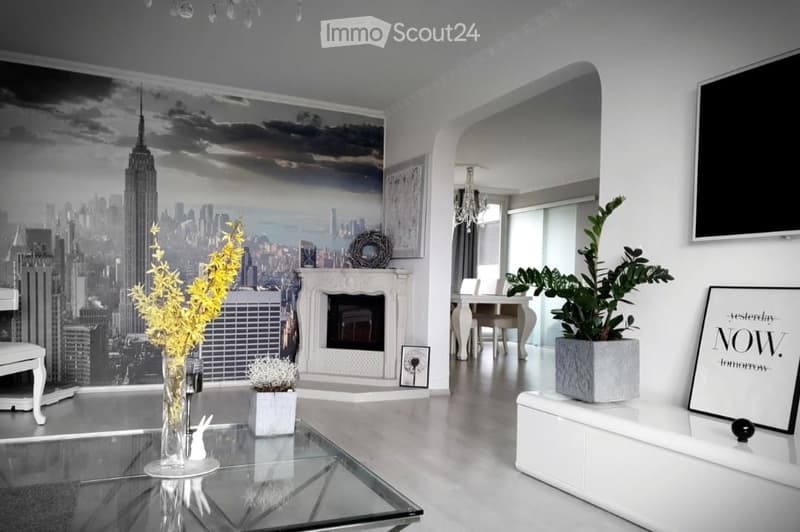 Modern living room with a large cityscape mural, fireplace, glass coffee table, white dining table, and television.