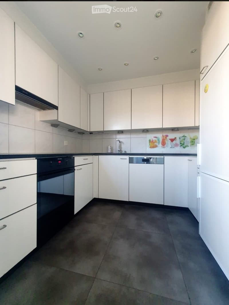Modern kitchen with white cabinets, dark tiled floor, built-in oven, dishwasher, and a decorative backsplash featuring colorful drink illustrations.