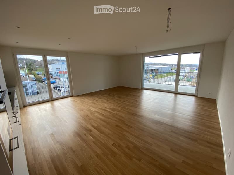 Empty room with light wooden flooring, large sliding glass doors leading to a balcony, and white walls.