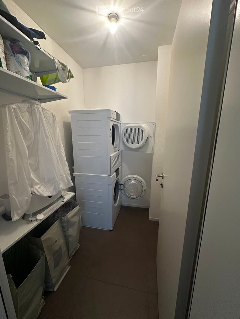 Laundry area with a washing machine, dryer, shelves, and trash bins.