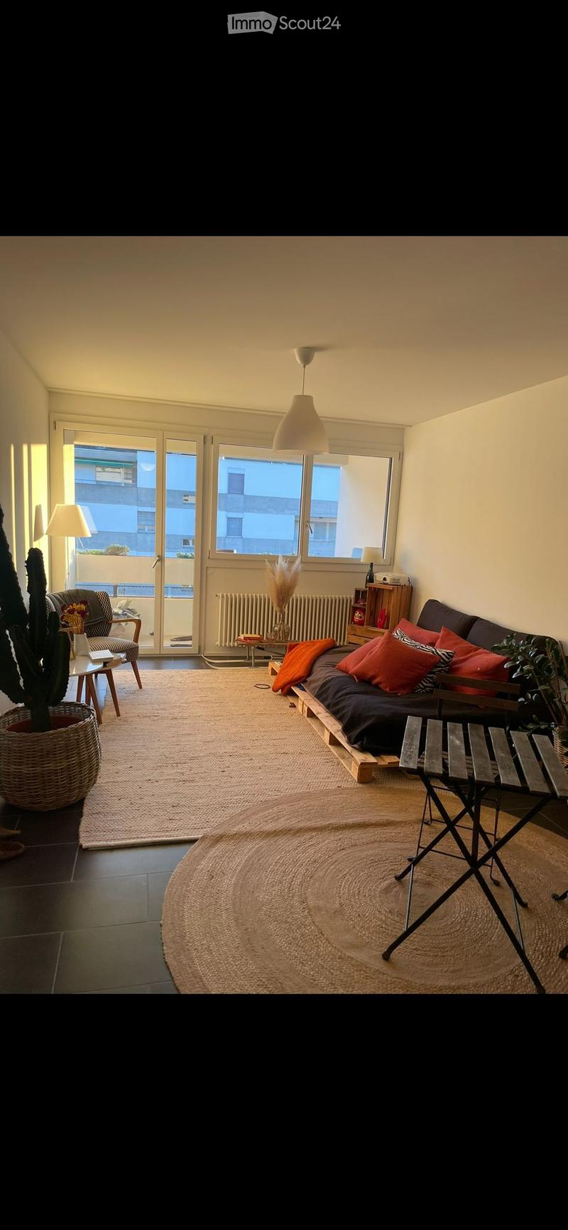 Modern living room with a sofa, chair, small table, and potted plant near a large window with a view of the balcony.