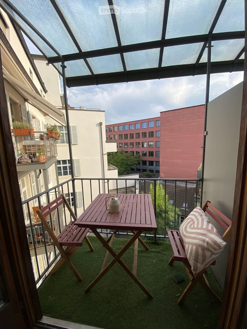 Balcony with artificial grass, wooden table, two chairs, and a decorative teapot.