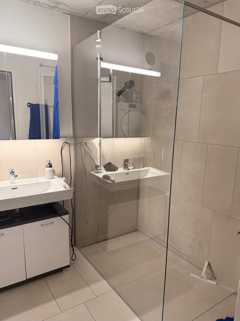 Modern bathroom with a white sink, mirrored cabinet, glass-enclosed shower, and beige tiled floor.