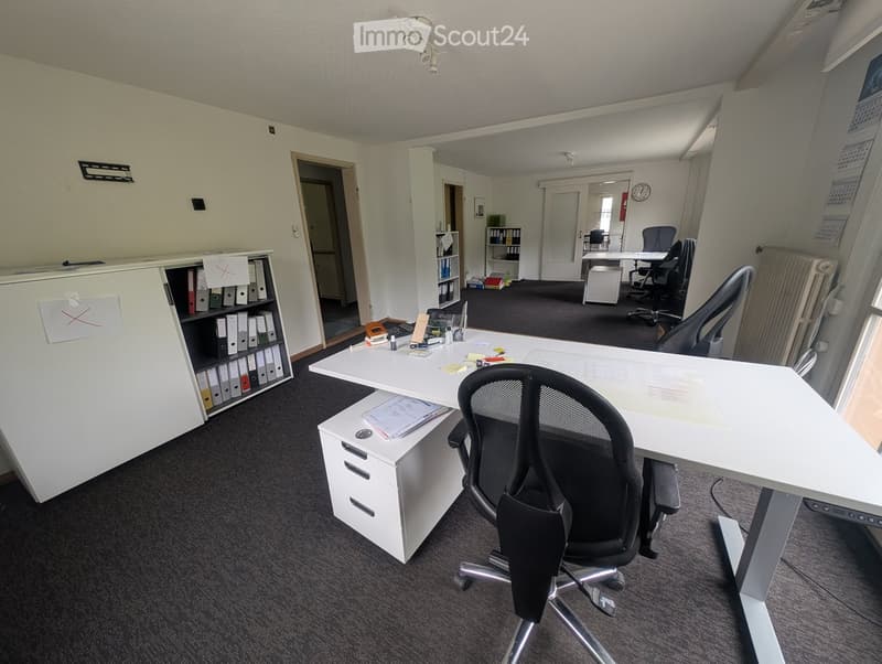 Office space with a large desk, ergonomic chair, filing cabinet, bookshelf, and additional workspace in the background.
