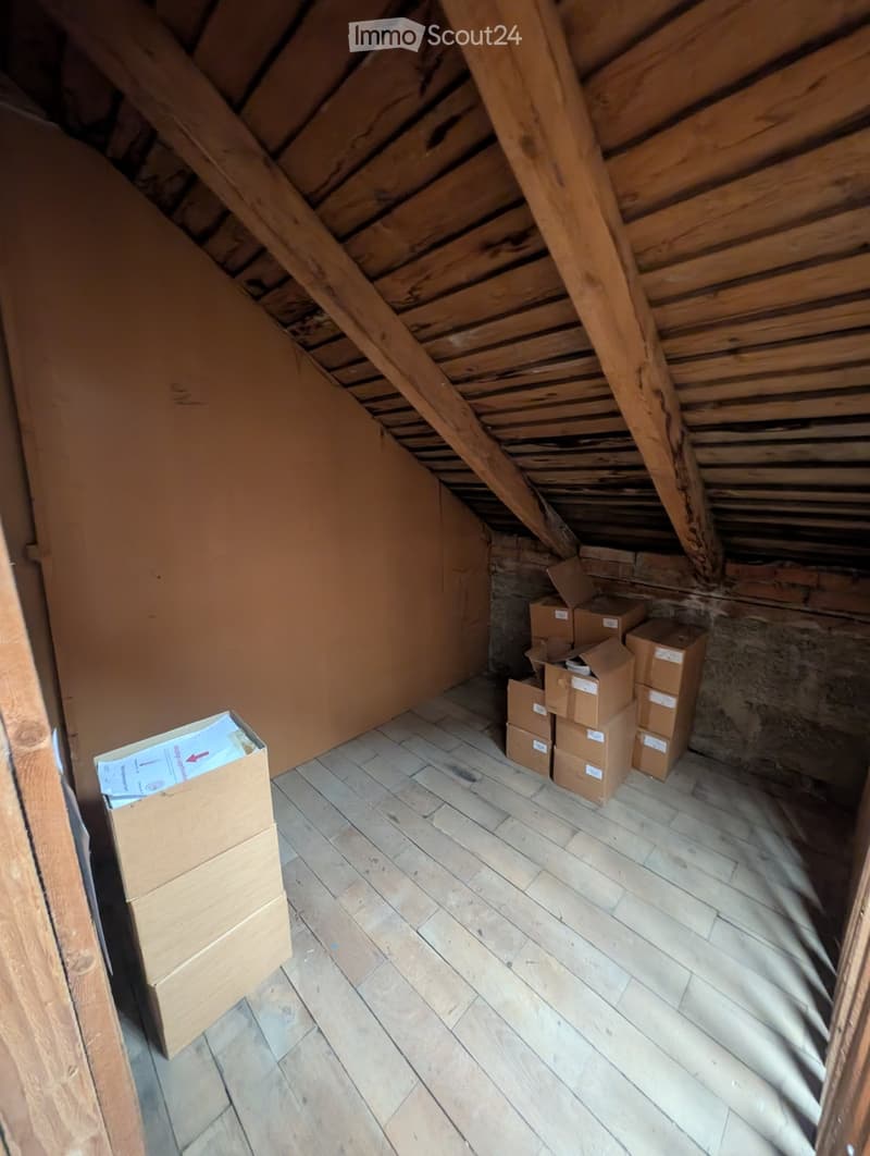 Empty attic space with wooden floor and exposed wooden beams, several cardboard boxes stacked in the corner.