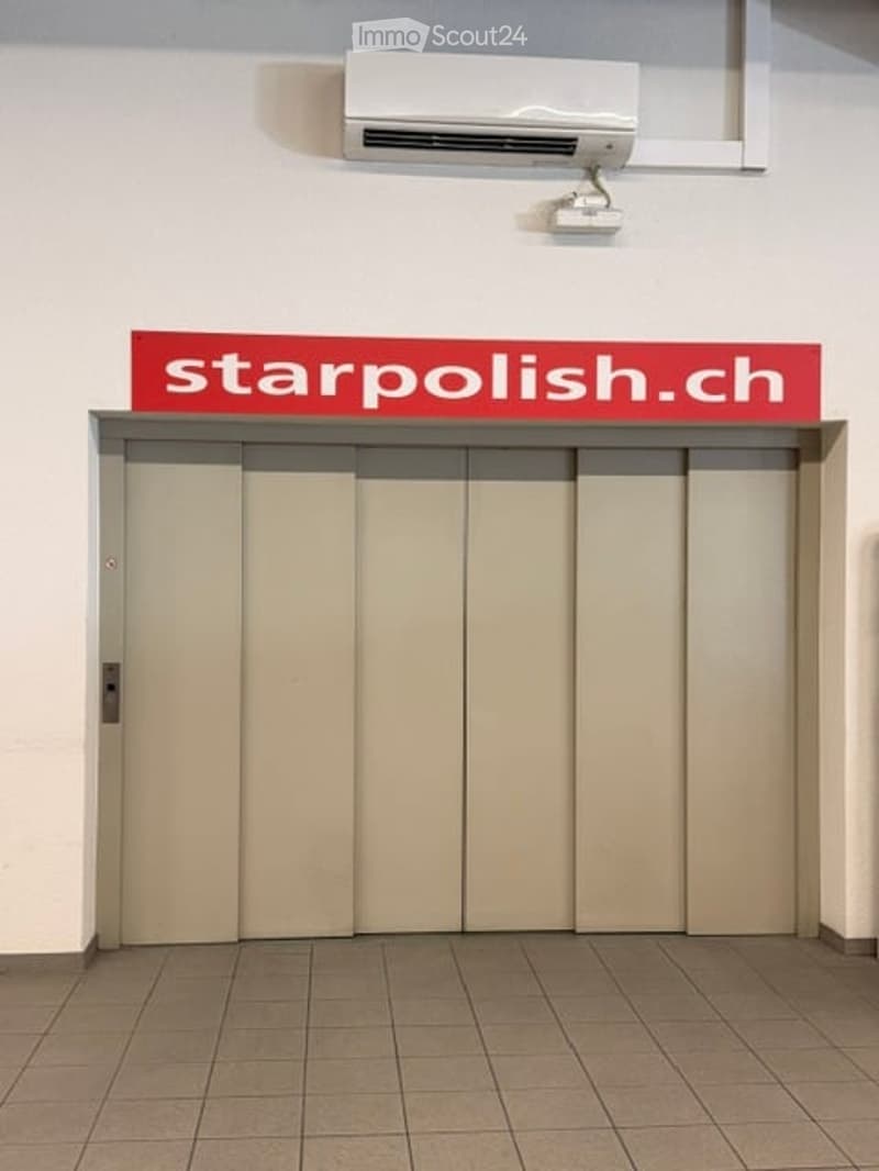Elevator entrance with a closed sliding door, a sign reading "starpolish.ch" above it, and an air conditioning unit mounted on the wall above.