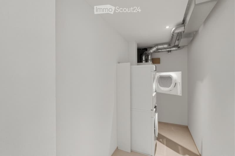 A small, clean utility room with white walls and a light-colored floor. Contains a washing machine and a dryer unit.