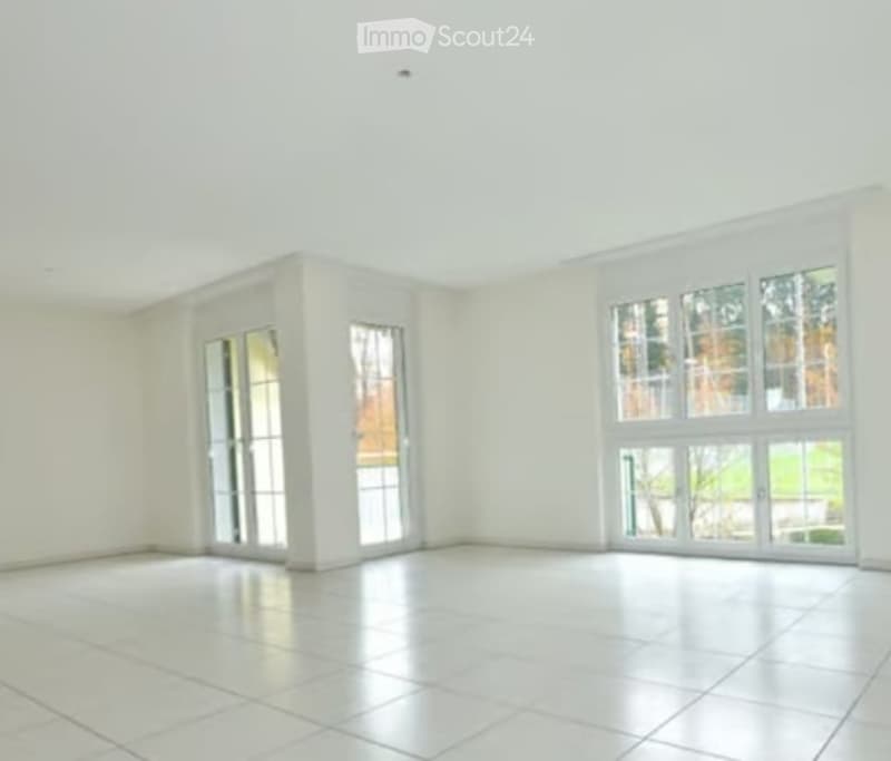Completely empty room with white walls, large windows, and white tiled flooring. No furniture or equipment.