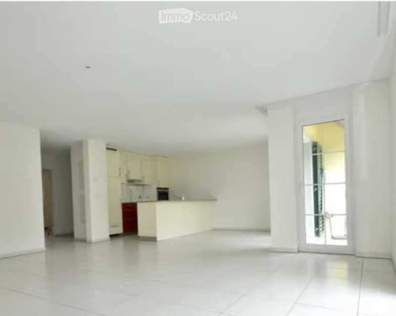 Bright, unfurnished kitchen with white cabinets, a red dishwasher, and a large glass door leading to a balcony.