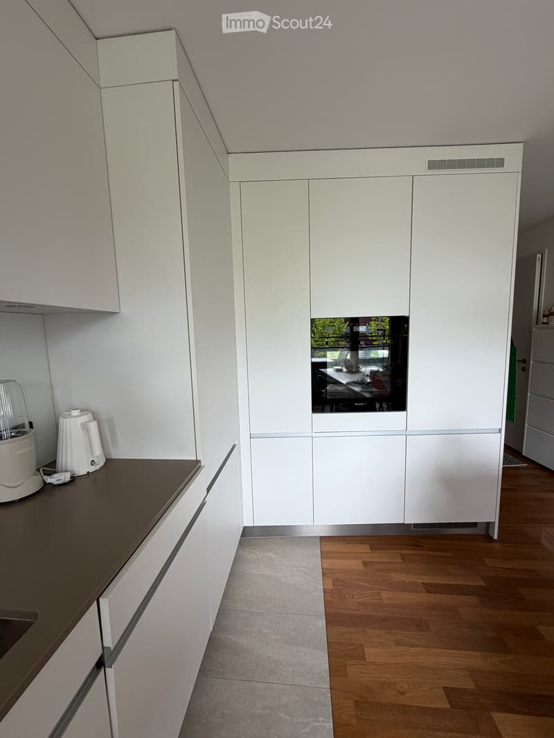 Modern kitchen with white cabinets, dark countertop, and wooden flooring. Visible appliances include a blender and a coffee maker on the counter.