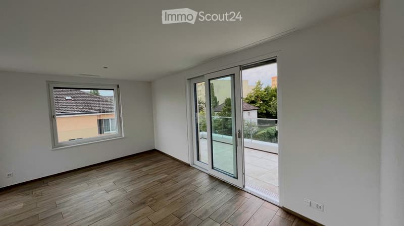 Empty room with wooden flooring, white walls, large window, and sliding glass door leading to a balcony.