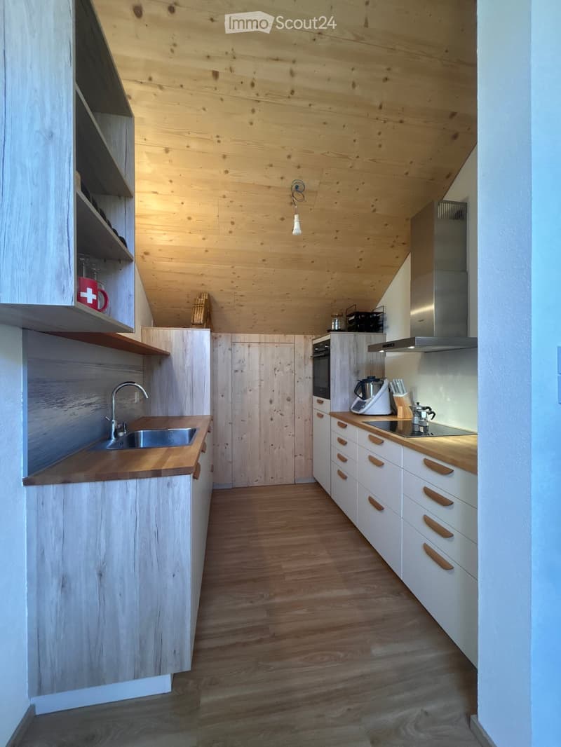 Modern kitchen with wooden cabinets, white walls, and a wooden ceiling. Features include a sink, oven, and various appliances on the counter.