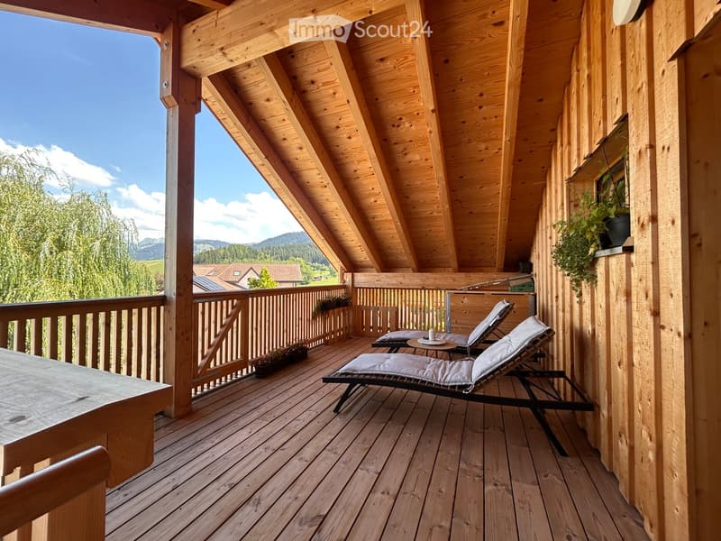 Wooden balcony with lounge chairs, small table, and scenic mountain view.