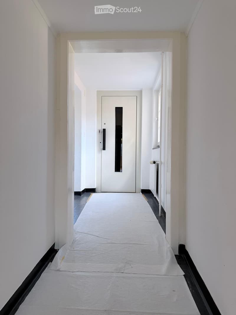 Empty hallway with white walls, a white door at the end, and a protective sheet covering the floor.