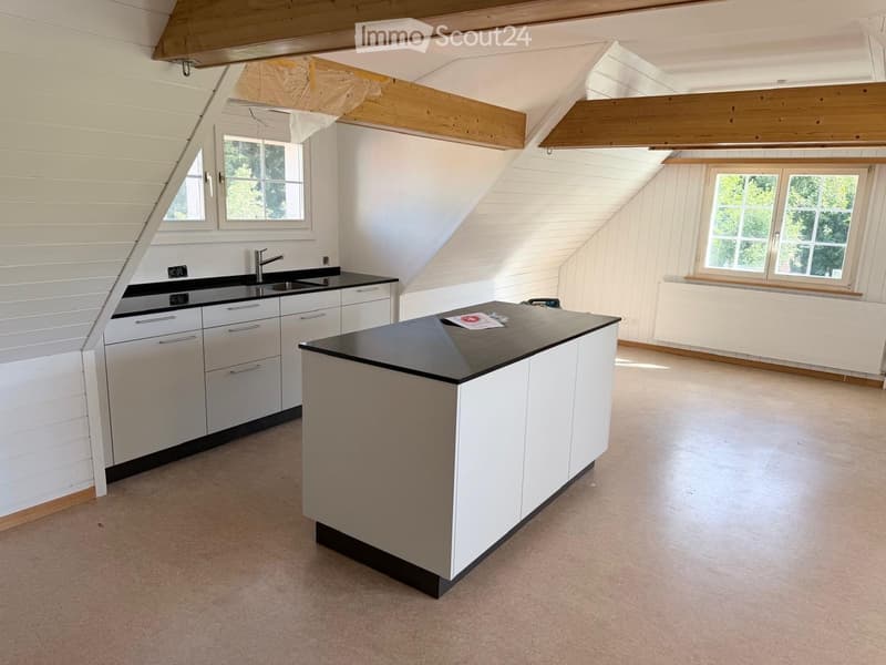 Modern kitchen with white cabinets, black countertops, and a central island. Features a sink with a modern faucet, large windows, and exposed wooden beams on the ceiling.