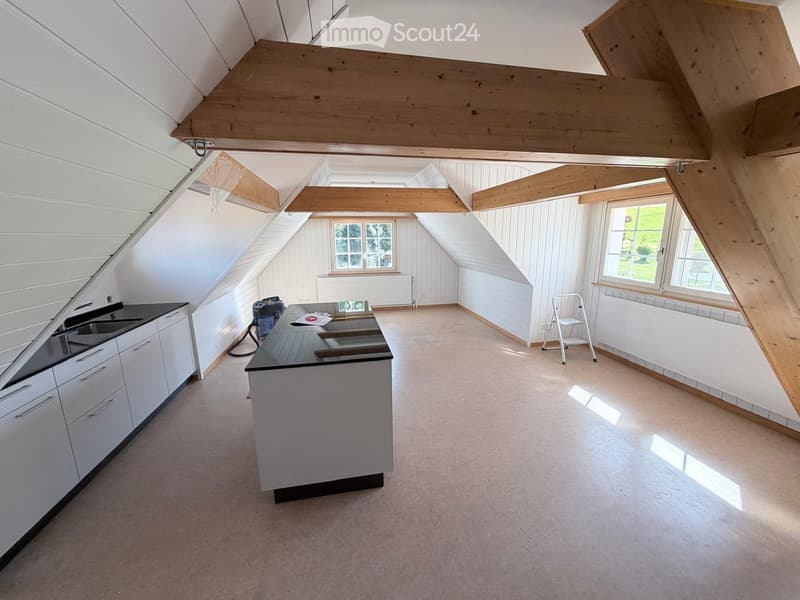 Modern kitchen with white cabinets, black countertop, and island in an attic space with exposed wooden beams and large windows.