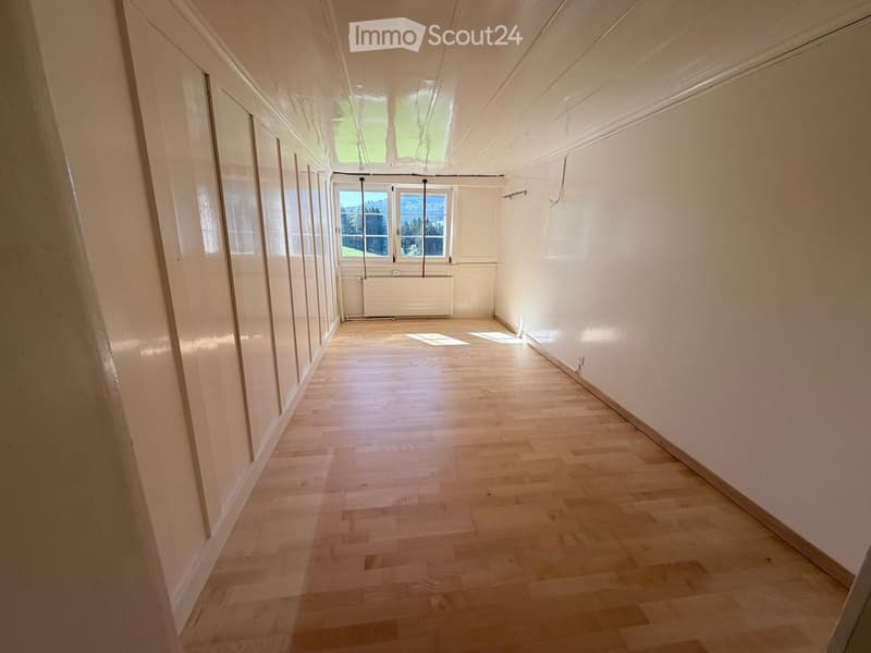 Empty hallway with wooden flooring, white walls, and large windows allowing natural light to enter.