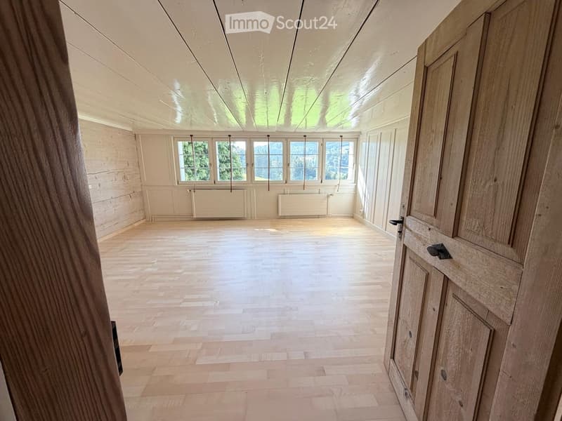 Empty room with wooden flooring, white walls, large windows, and wooden cabinetry.