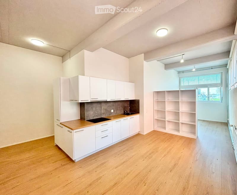 Modern kitchen with white cabinets, wooden countertop, sink, and built-in shelves. Light wooden flooring and large window with blinds.