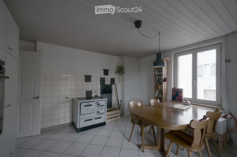 Bright kitchen with white cabinets, tiled walls, a round wooden dining table with chairs, and a stove.
