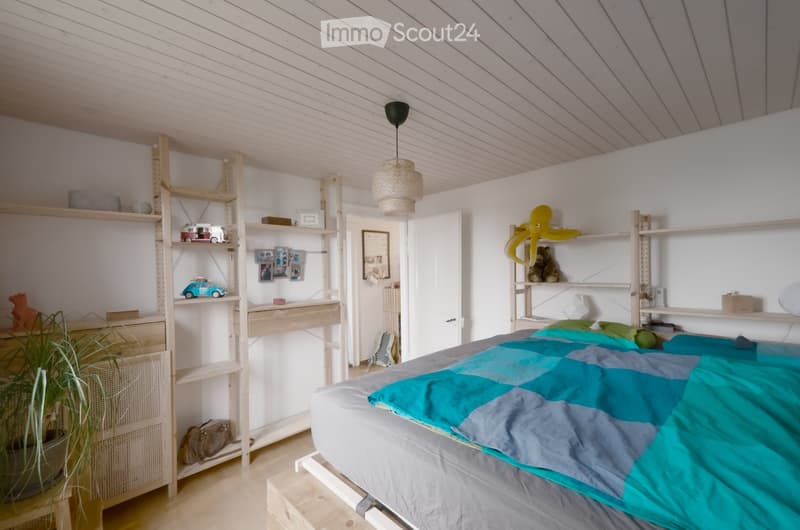 Bright, modern bedroom with a lofted bed, wooden shelves, and decorative items including a toy car, octopus toy, and framed photos.