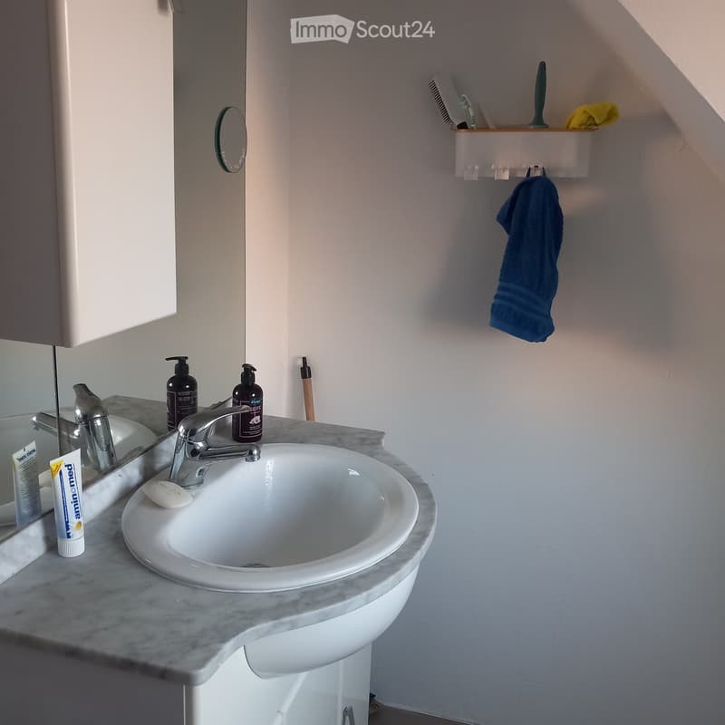 Modern bathroom with a white sink, chrome faucet, mirror, and toiletries on the counter. A blue towel hangs on the wall.