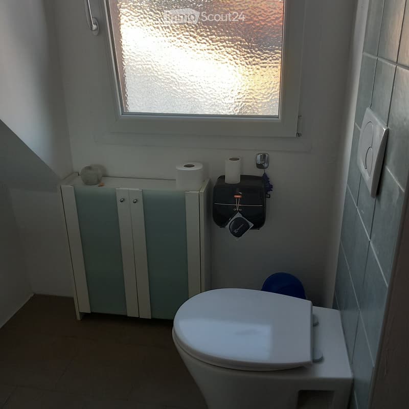 Modern bathroom with a toilet, toilet paper holder, and a small cabinet with a glass bowl on top.