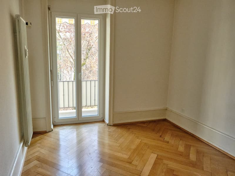 Empty room with wooden parquet flooring, light-colored walls, and a large glass door leading to a balcony with a metal railing.