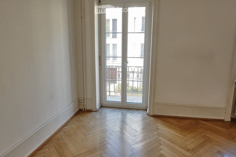 Empty room with wooden herringbone flooring, light-colored walls, and a large glass door leading to a balcony.