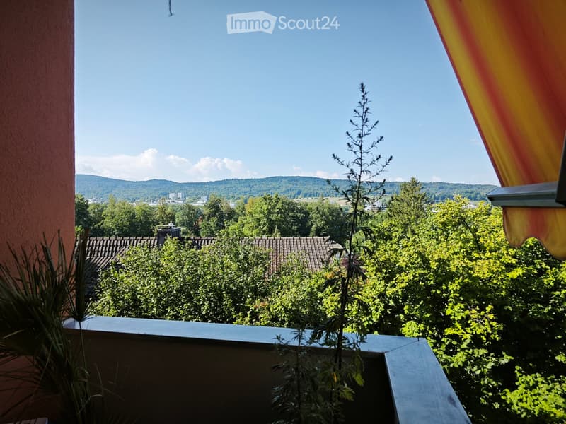Balcony with a view of a lush green landscape, trees, and distant hills under a clear blue sky.
