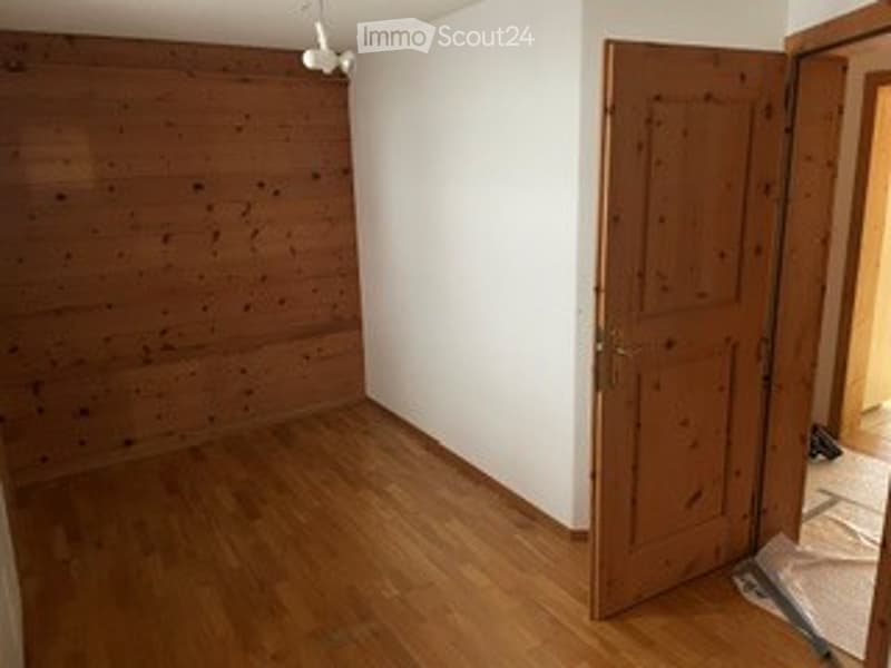 Empty room with wooden walls and floor, a closed wooden door, and a small open doorway leading to another area.