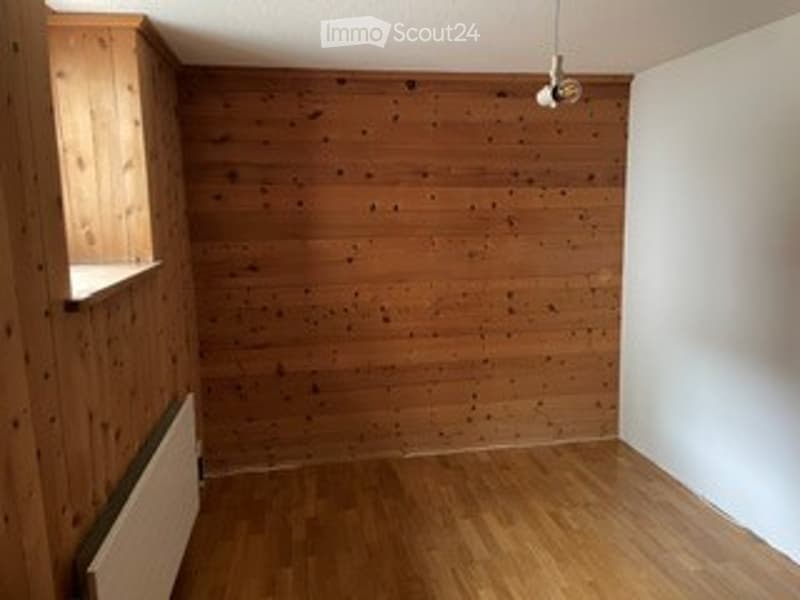 Completely empty room with wooden walls and floor, white wall on one side, radiator, and a window with a wooden frame.