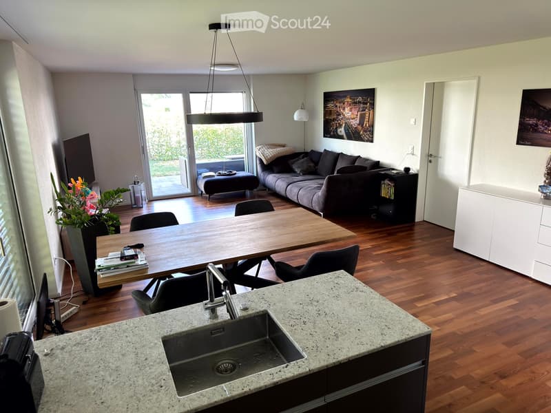Open-plan living and dining area with a sofa, coffee table, dining table, chairs, and a kitchen sink.