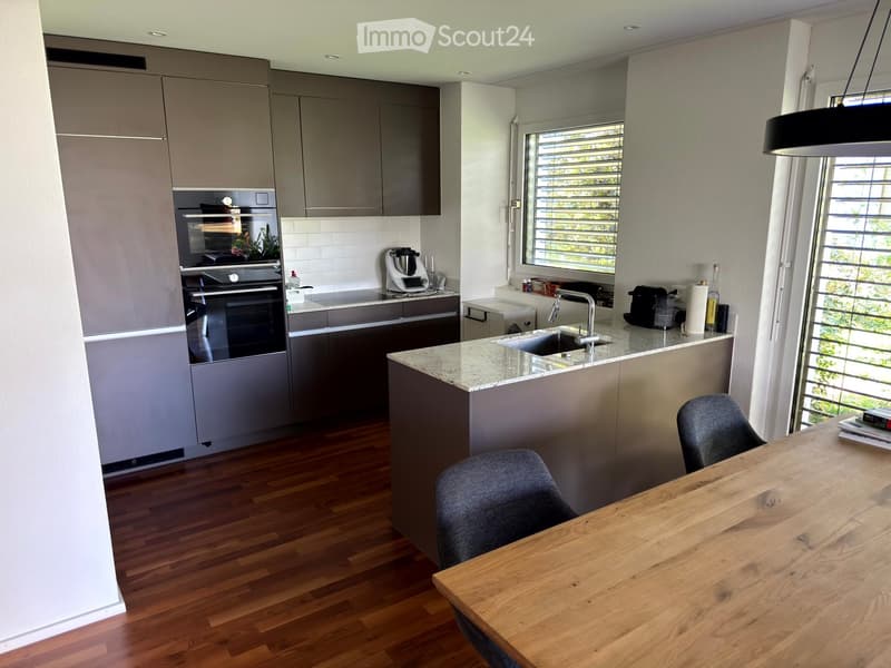 Modern kitchen with grey cabinets, a central island with a marble countertop, a wooden dining table, and two chairs.
