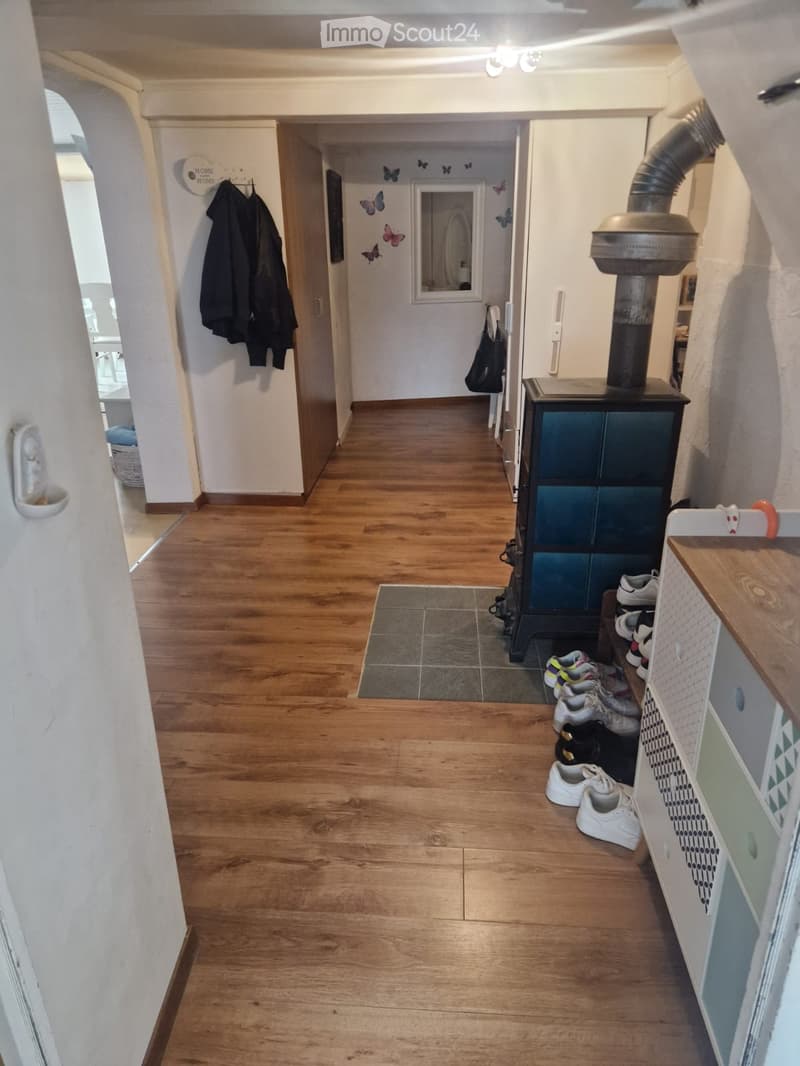 Hallway with wooden flooring, coat rack, shoe storage, and a wood-burning stove. Butterfly wall decals visible on the wall.
