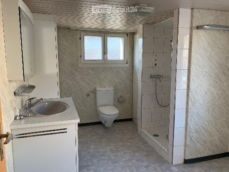 Modern bathroom with a marble-patterned wall, a white toilet, a sink with a chrome faucet, and a glass-enclosed shower stall.