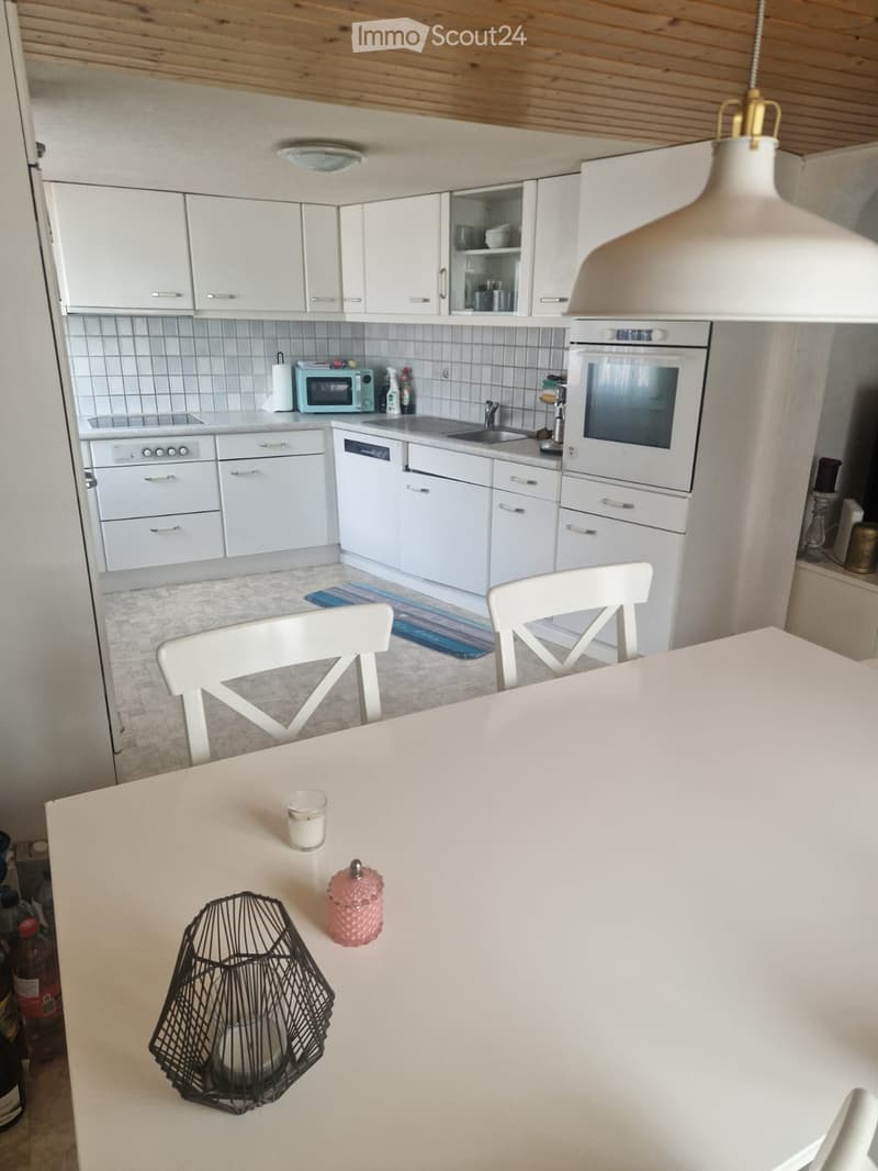 Bright kitchen with white cabinets, a central island table, and modern appliances including an oven, microwave, and dishwasher. The space features a pendant light and a small rug on the floor.