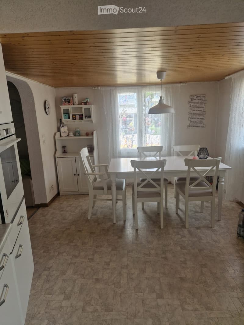 Dining room with a white dining table and four chairs, a cabinet with shelves, an oven, and a hanging lamp.