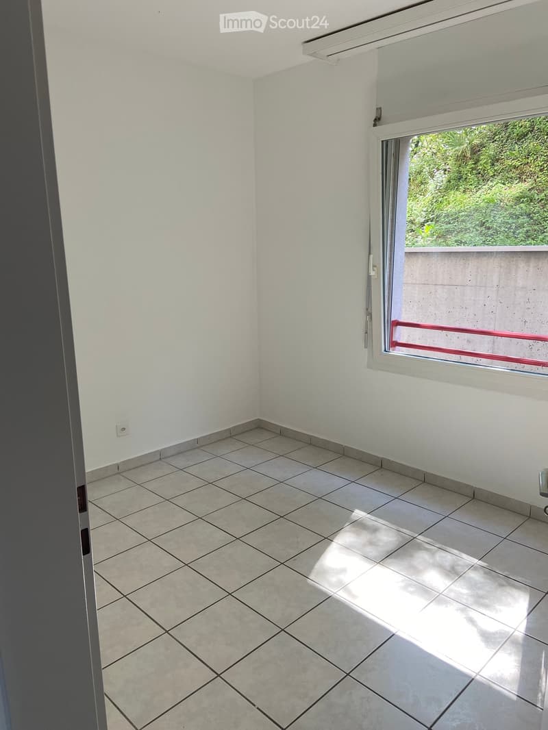 Empty room, white walls, tiled floor, sliding window, balcony access, power outlet on the wall, bright sunlight coming through the window