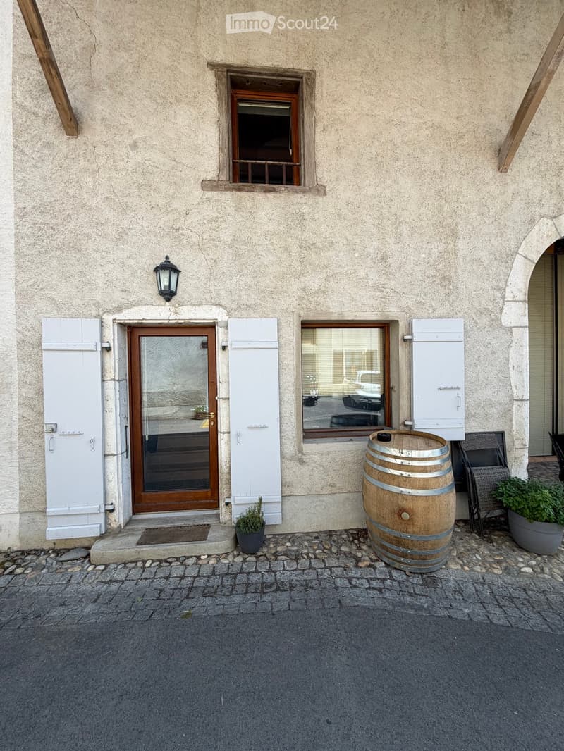 Facade of a building with a wooden door, windows, a barrel, and potted plants.