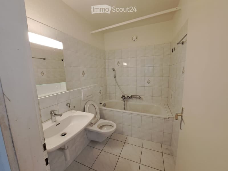 Bathroom with white tiled walls and floor, featuring a sink, toilet, bathtub, and mirror.