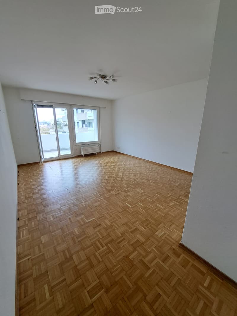 Empty room with wooden herringbone flooring, white walls, and a large sliding glass door leading to a balcony.