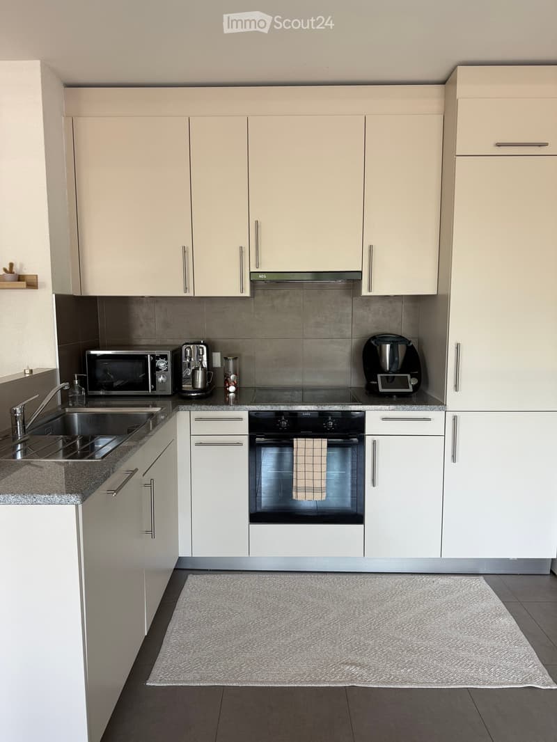 Modern kitchen with white cabinets, stainless steel appliances, granite countertops, and a gray tiled backsplash.